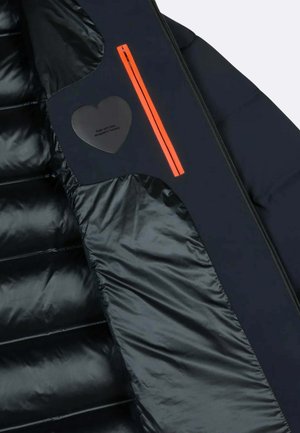 Interno di una giacca puffer blu navy con sezioni trapuntate orizzontali, tasca con zip arancione brillante e etichetta nera a forma di cuore con la scritta "Fatto con amore".