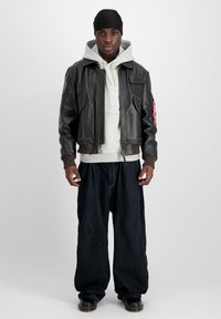 Brun läderbomberjacka med ribbade manschetter, grå huvtröja och lösa mörkblå denimbyxor. Svarta skor fulländar outfiten.