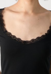 Camiseta sin mangas negra con un escote pronunciado, que presenta un delicado ribete de encaje alrededor del cuello. Textura de tela suave, diseño ajustado.