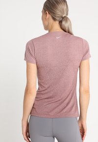 Camiseta atlética de manga corta en rosa polvoriento con una textura jaspeada. Cuenta con un sutil logo de Nike en la parte posterior del cuello.