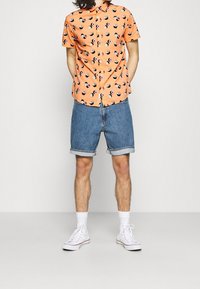 Short-sleeve orange shirt with sushi print, paired with rolled denim shorts. White sneakers and ankle socks complete the outfit.