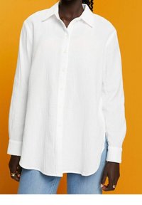 Chemise blanche à boutons, en tissu texturé, avec un col pointu et des manches longues, assortie à un jean bleu clair.