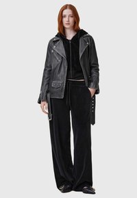 Svart läderbikerjacka med silverdetaljer, ovanpå en svart kort hoodie och svarta vida byxor i mjukt material.