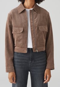 Brown corduroy cropped jacket with two chest pockets, a front zipper, and a point collar, paired with dark denim jeans.