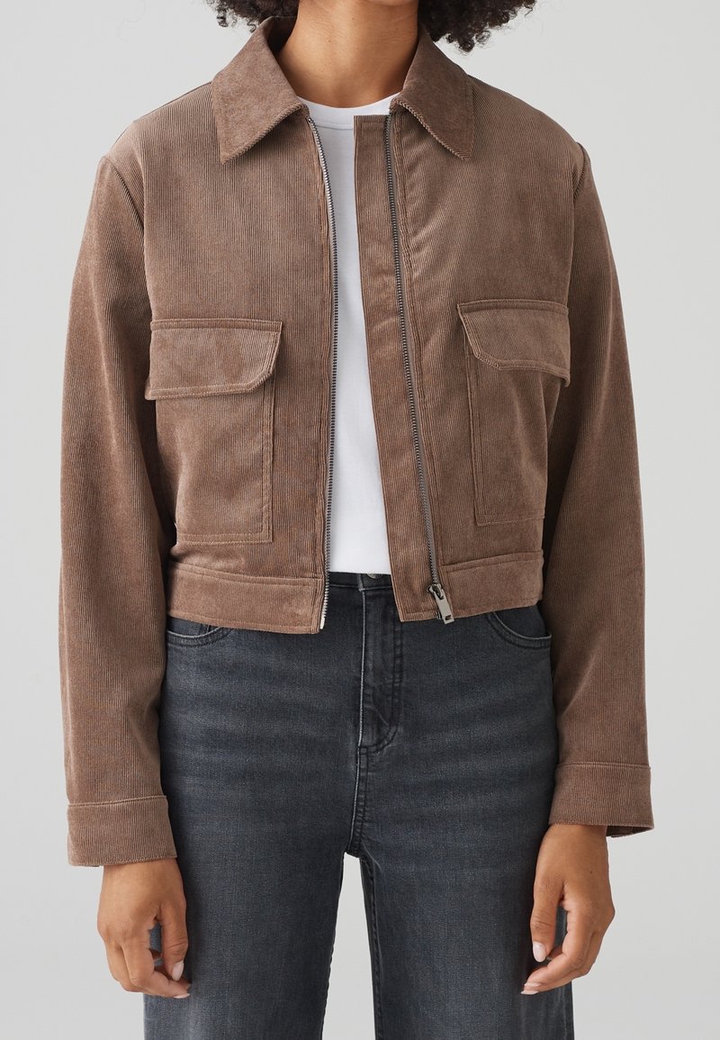 Brown corduroy cropped jacket with two chest pockets, a front zipper, and a point collar, paired with dark denim jeans.