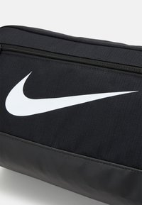 Black Nike sports bag with a textured fabric, featuring a prominent white swoosh logo and a zip closure along the top.