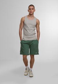 Graues Tanktop, grüne Shorts mit Logo, weiße Turnschuhe und weiße Socken. Lässige Sportbekleidung, eng anliegendes Tanktop und lockerer Schnitt bei den Shorts.