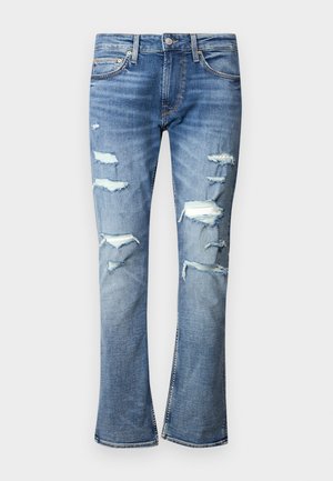 Light blue ripped jeans with multiple distressed patches. Flared leg design with a smooth texture and contrast stitching. Metal button closure.