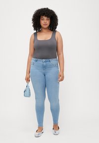 Monosuit gris con escote cuadrado, combinado con jeans ajustados de color azul claro. Unos zapatos planos plateados y un pequeño bolso azul completan el look.