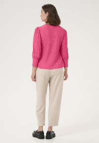 Blouse texturée fuchsia avec des manches bouffantes trois quarts, associée à un pantalon beige fuselé et des chaussures à plateforme noires.