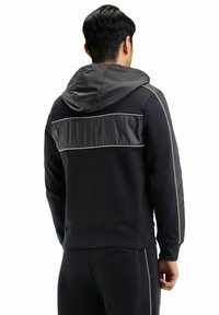 Hoodie noir avec un panneau gris brillant dans le haut du dos, des coutures blanches contrastantes et une capuche à cordon.