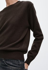 Brązowy sweter z miękkiego materiału, z okrągłym dekoltem i długimi rękawami. Dół swetra jest wykończony ściągaczem, a ogólny fason jest luźny.