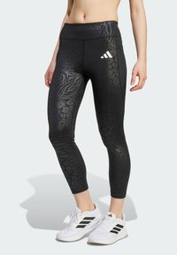 Leggings sportivi neri con un design a stampa animale testurizzato, elastico alto in vita e logo Adidas bianco sulla coscia sinistra.