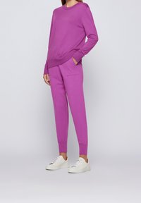 Person klädd i en matchande lila sweatshirt med lång ärm och joggers med fickor, i kombination med vita låga sneakers.