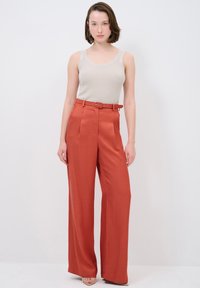 Red high-waisted trousers with a belt and pleated front, paired with a fitted beige tank top. Smooth fabric texture, wide-leg design.
