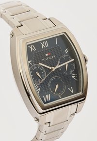 Ασημένιο ρολόι χειρός Tommy Hilfiger με μαύρο καντράν, ρωμαϊκούς αριθμούς, τρεις μικροκλήσεις που εμφανίζουν ώρα 24 ωρών, ημέρα και ημερομηνία.