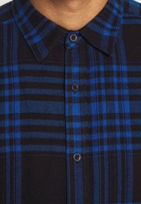 Camicia a quadri in tonalità di nero e blu, con colletto button-down e bottoni neri. Tessuto morbido con motivo a quadri strutturato.