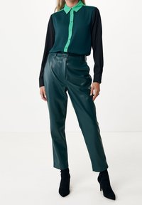 Teal and black long-sleeve blouse with a green collar, paired with glossy green faux leather trousers and black ankle boots.