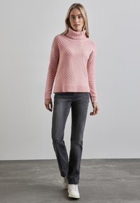 Ljust rosa, strukturerad tröja med hög polokrage, ribbade ärmslut och nederkant. I kombination med grå raka jeans och vita sneakers.