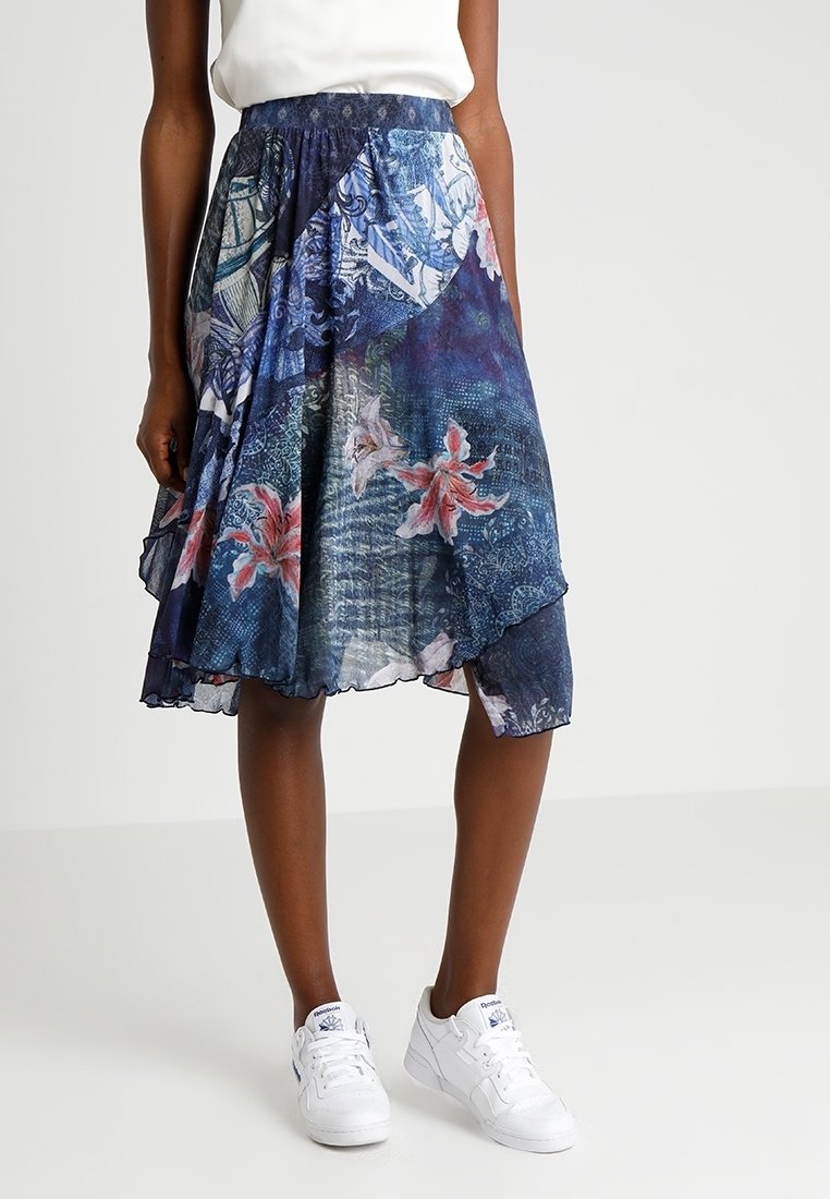 Knälång kjol med blommönster i blå toner, tillverkad av lätt tyg med en volangkant. Kombinerad med vita sneakers.