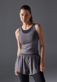 Grå trenings t-skjorte med rund hals lagt over en svart topp, kombinert med grå shorts med elastisk midje og svarte leggings.