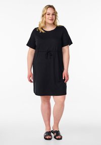 Musthave lühikeste varrukatega must kleit ümmarguse kaelusega, kummipaelaga vööl ja pehme tekstuuriga, mille juurde kuuluvad mustad libisemisjalatsid nTermandsükkadega.
