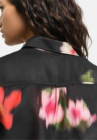 Camicia nera con un motivo floreale in tonalità di rosa e verde. Il retro presenta un colletto e una texture delicata.