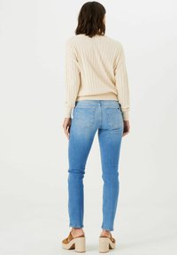 Suéter crema de canalé con cuello redondo, combinado con jeans ajustados de color azul claro. La persona lleva sandalias plataforma de color marrón, posando de espaldas.