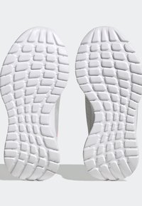 Suole di scarpe sportive bianche con un motivo testurizzato, caratterizzate da profonde scanalature e sezioni rialzate per la trazione, bordi lisci e un design minimalista.