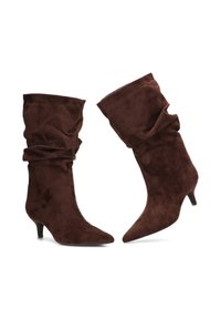 Botines de ante marrón con diseño holgado, punteras puntiagudas y tacones de aguja, que presentan una textura suave y un brillo sutil.