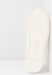 Suola di sneaker in gomma bianca con grip testurizzato, caratterizzata da strisce orizzontali e diagonali, logo impresso e un design elegante e minimalista.