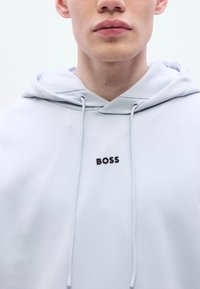 Ανοιχτό μπλε φούτερ με κουκούλα από απαλό ύφασμα, με τσέπη καγκουρό, κορδόνια και μαύρο λογότυπο "BOSS" στο στήθος. Ομαλή υφή.