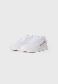 White sneakers with a smooth synthetic upper, flat laces, and a rubber sole. Features a red and blue stripe on the side.