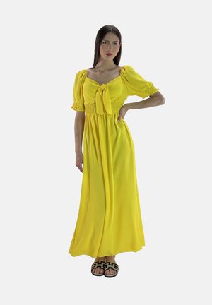 Robe maxi en tissu jaune vif, avec des manches bouffantes, un détail à nouer à l'avant et une taille smockée. Associée à des sandales noires à motifs.