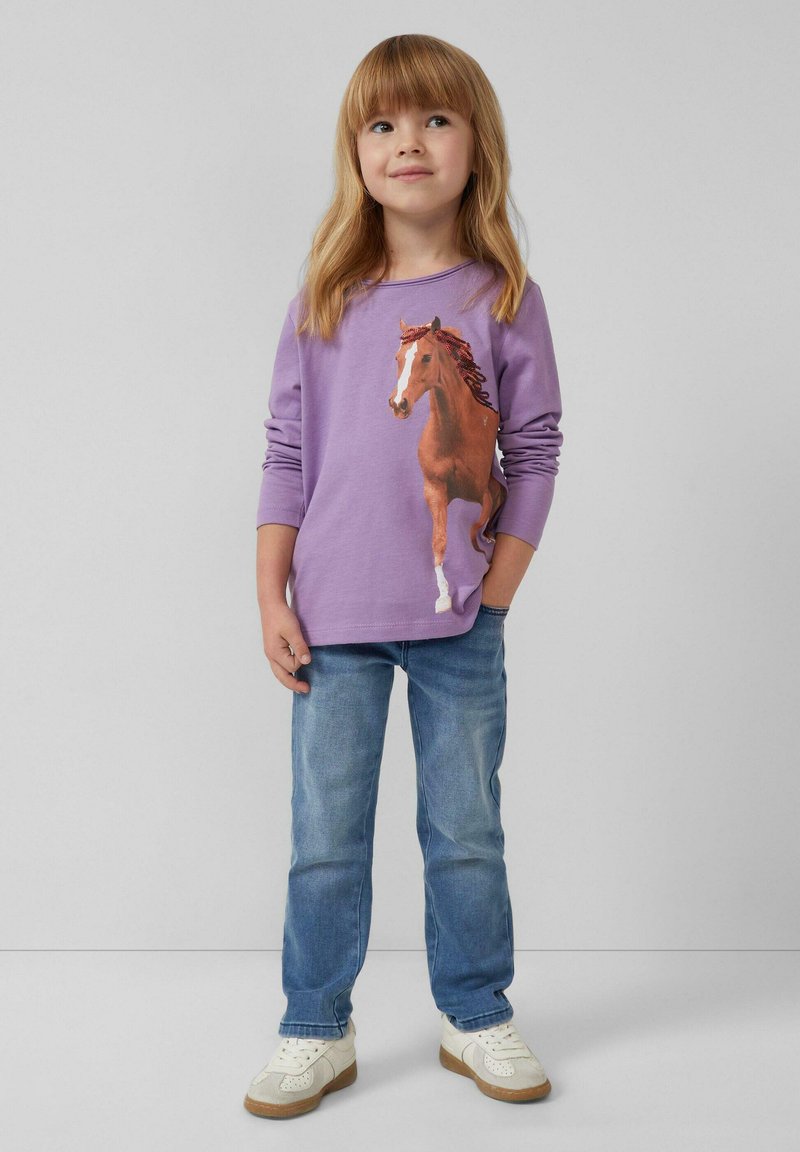 Paarse lange mouwen shirt met een bedrukt bruin paardenontwerp, gecombineerd met lichtblauwe jeans en witte sneakers met rubberen zolen.