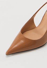 Pompe slingback en cuir verni marron avec un bout pointu et une texture lisse. Présente un design de côté découpé et une semelle minimaliste.