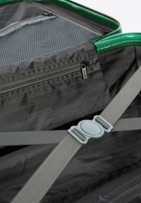 Zelená cestovní taška uvnitř s šedým podšíváním, obsahující kapsy na zip a nastavitelné popruhy. Texturovaná tkanina s jemnými detaily značky.
