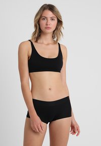 Musta urheilusukka ja vastaavat sortsit, jotka on valmistettu sileästä, joustavasta kankaasta. Sporttisukalla on leveä ympyräkaula-aukko ja kapeat hihnat.