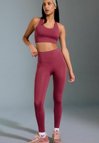 Reggiseno sportivo bordeaux e leggings a vita alta, realizzati in tessuto elasticizzato, texture liscia, con cuciture minime e una fascia abbinata.