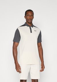 Polo para hombre en color beige claro y gris oscuro. Cuenta con collar, manga corta y un logo de Nike en el pecho. Hecho de tejido transpirable.