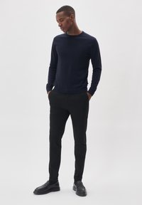 Mornarska sv sweater iz mehkega blaga, okrogla izreza, dolgi rokavi. Ujemite z črnimi hlačami in črnimi loaferji, stoji z rokami v žepih.
