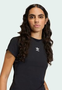 Čierne bavlnené tričko s krátkymi rukávmi a okrúhlym výstrihom, s bielym logom Adidas na hrudi. Hladká textúra a priliehavý strih.