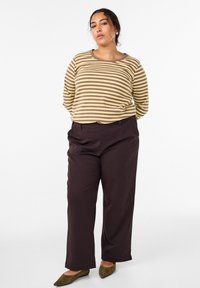 Beżowa i brązowa pasiasta bluzka z długim rękawem, w połączeniu z szerokimi spodniami w ciemnym brązie. Modelka ma na sobie oliwkowe baleriny. Ogólnie prosty, luźny krój.