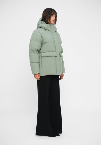 Light green puffer jacket with a hood, featuring a front closure, two large patch pockets, and a relaxed silhouette. Worn over black wide-leg pants.