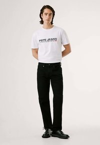 Balti medvilninė marškinėliai su juodu „PEPE JEANS“ logotipu, derinami su juodais džinsais iš dažyto džinso, turinčiais tiesų kojų kirpimą, ir juodais batais.