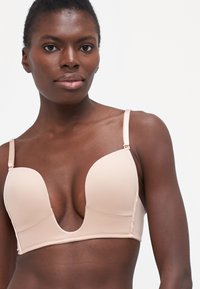 Nud plunge-bh med glatte, formede kopper og justerbare stropper; har minimalistisk design og sømløs tekstur.