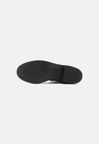 Suela de zapato de goma negra con patrón de agarre texturizado, con forma redondeada y una ligera sección de tacón para una mayor estabilidad.