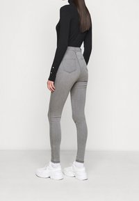 Vaqueros skinnys grises de cintura alta con una textura suave, dos bolsillos traseros y un diseño ajustado. Combinados con deportivas blancas.