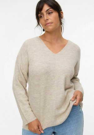 Pull en V beige avec texture côtelée et manches longues, associé à un jean déchiré bleu clair. Matière douce et coupe décontractée.
