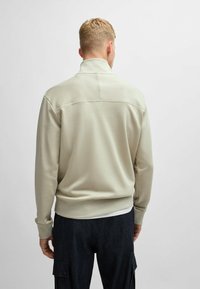 Felpa con zip beige chiaro, colletto alto, polsini e orlo a coste. Tessuto liscio con un pannello superiore a contrasto sul retro.